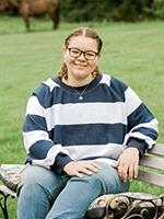 Girl wearing glases  and a stripped blue and white shirt with curly light brown hair.